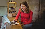 Woman sitting at counter and using laptop in bicycle shop