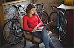 Woman sitting on chair and using laptop in bicycle shop
