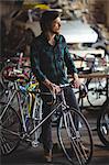 Thoughtful mechanic standing with bicycle in bicycle shop