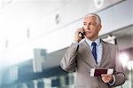 Businessman with passport and airplane ticket talking on cell phone in airport