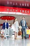 Business people leaving airport duty free shop with shopping bags and suitcase