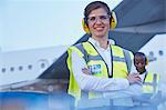 Portrait smiling female air traffic controller standing near airplane