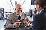 Smiling businessman giving passport to customer service representative at airport check-in counter