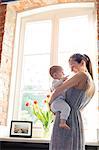 Mother holding baby daughter at window