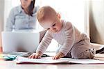 Baby girl playing on floor near mother working on laptop