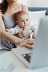 Mother holding baby daughter and working at laptop