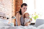 Mother holding daughter and working at laptop on bed