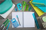 Open spiral notebook with colorful stationery and school equipment on wooden surface.