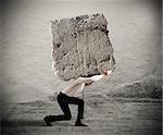 Businessman walking with a heavy boulder on his back