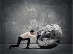 Businessman pushing a heavy boulder with great effort