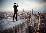 Businessman looks at the city from the roof with binoculars