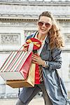 Stylish Christmas in Paris. Portrait of smiling trendy woman with shopping bags and Christmas present box in Paris, France