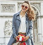 Stylish Christmas in Paris. Portrait of happy young woman in sunglasses with shopping bags and Christmas present in Paris, France