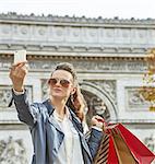 Stylish autumn in Paris. young woman in trench coat in Paris, France taking selfie with cellphone with shopping bags
