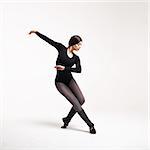 young beautiful woman dancer in black swimsuit posing on a light grey studio background