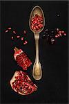 Delicious ripe pomegranate seeds with silver spoon on black background, top view. Healthy exotic fruit eating.