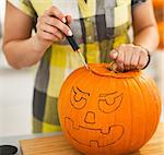 Frightful Treats on the way. Closeup on housewife in the Halloween decorated kitchen carving a big orange pumpkin Jack-O-Lantern