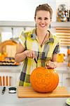 Frightful Treats on the way. happy young woman in the Halloween decorated kitchen carving a big orange pumpkin Jack-O-Lantern