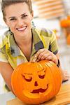 Frightful Treats on the way. Portrait of smiling young woman in the Halloween decorated kitchen with a big orange pumpkin Jack-O-Lantern