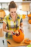Frightful Treats on the way. happy young woman in the Halloween decorated kitchen prepare big orange pumpkin for carving