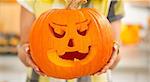 Frightful Treats on the way. Smiling modern housewife in the Halloween decorated kitchen showing big pumpkin Jack-O-Lantern. Closeup