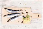 Delicious anchovies fish with peppercorns and fresh herbs on wooden chopping board on white wooden background, top view..