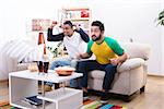 Image of friends men watching football game, screaming and shouting, drinking alcohol drinks and eating pop corn at home.