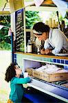 Woman leaning over the counter of a mobile coffee shop, talking to girl.