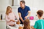 A family of four people, parents and two children preparing breakfast in the kitchen.