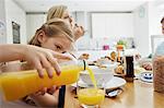 A family seated at breakfast, a girl pouring a glass of orange juice.