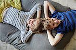 A family home.  A boy and girl lying on the sofa with their heads close together. View from above.