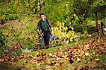 A gardener using a leaf blower to clear up autumn leaves in a garden.
