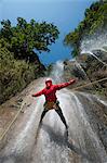 A man pauses to hold his arms in the falling water while canyoning, Nepal, Asia