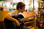 Young boy strumming an acoustic guitar inside a music shop.