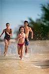 Happy family running along a tropical beach in the shallows.