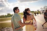 Young couple walk with their arms around each  other on airport tarmac.