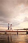 Happy mid adult couple walking hand in hand along a pier.