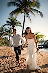 Playful young newlywed couple walking along a beach after their wedding.