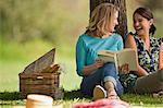 Happy friends reading a book together under a tree at the park.