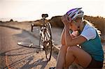 Young female cyclist sitting roadside with her head in her hands