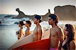 Teenagers standing on the beach in a row carrying surfboards, El Salvador.