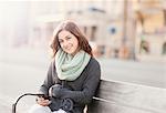 Portrait of young woman sitting on bench using phone