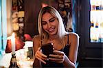 Beautiful smiling woman using mobile phone in bar