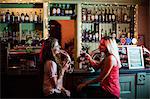 Women interacting while having a glasses of wine at counter in bar
