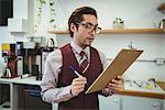 Man writing with pen on clipboard in coffee shop