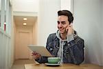 Man talking on mobile phone while holding digital tablet in coffee shop