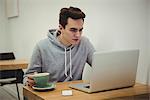 Man looking at laptop while holding coffee cup in coffee shop