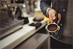 Mid-section of man holding portafilter with ground coffee in coffee shop