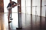 Ballerina stretching at barre in ballet studio