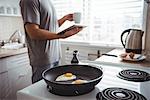 Man using digital tablet while preparing fried eggs in the kitchen at home